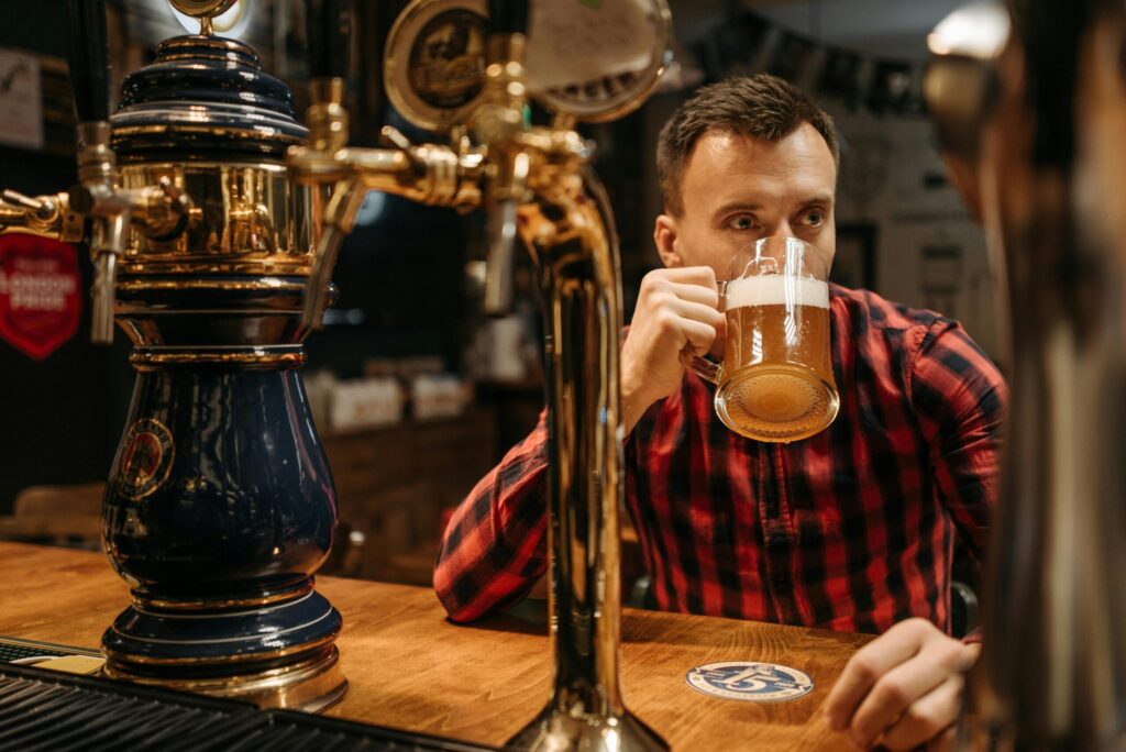 A man sipping beer from a mug at a pub with vintage beer taps, in a relaxed atmosphere.